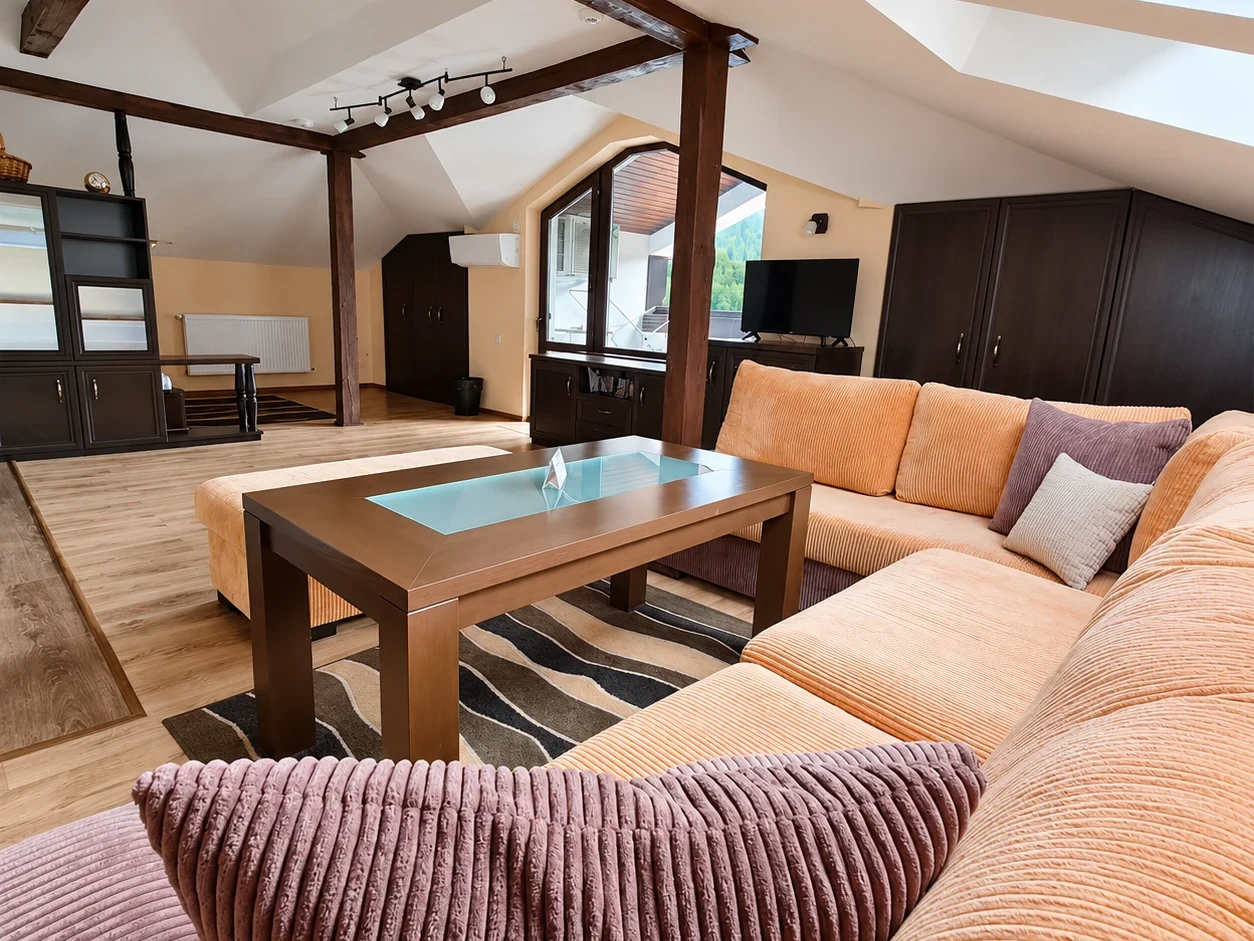 A corner sofa with cushions, a low table with a glass inlay and wooden beams under the sloping ceiling