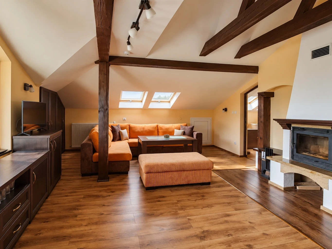 The Deluxe Apartment's living room under wooden beams: a corner sofa under the roof windows, a TV and the fireplace