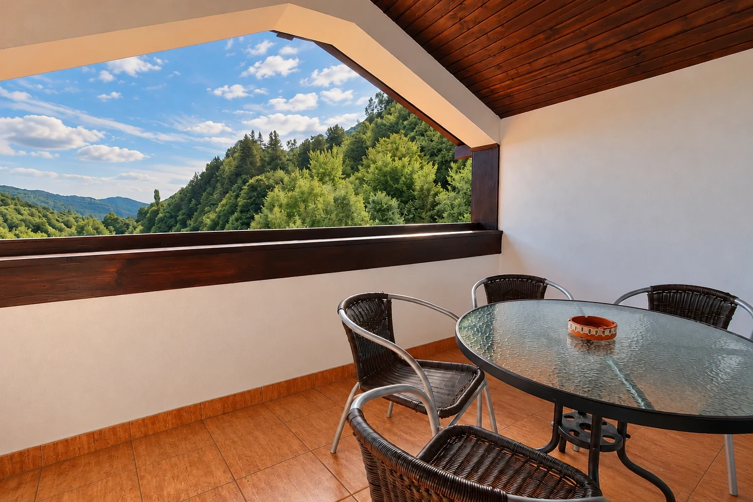 The Deluxe Apartment's covered balcony, with a table, chairs and a view of the wooded hills