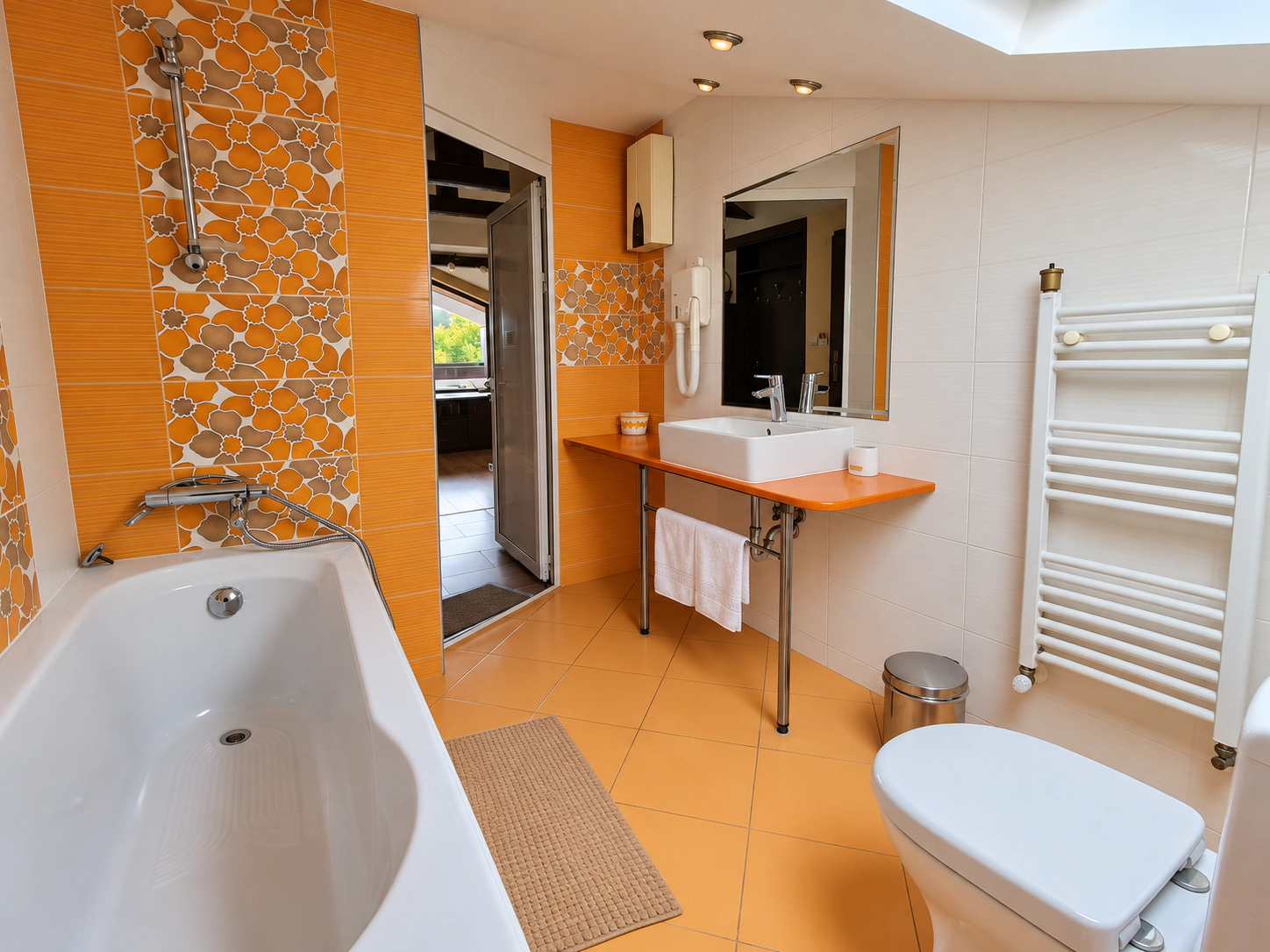 The Deluxe Apartment's bathroom with a bathtub, a basin on an orange counter and a towel rail
