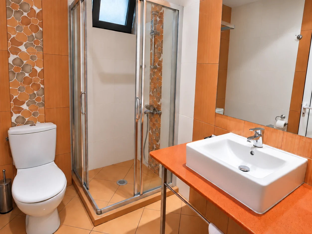 A shower cubicle, a basin on an orange counter and a decorative band of tiles