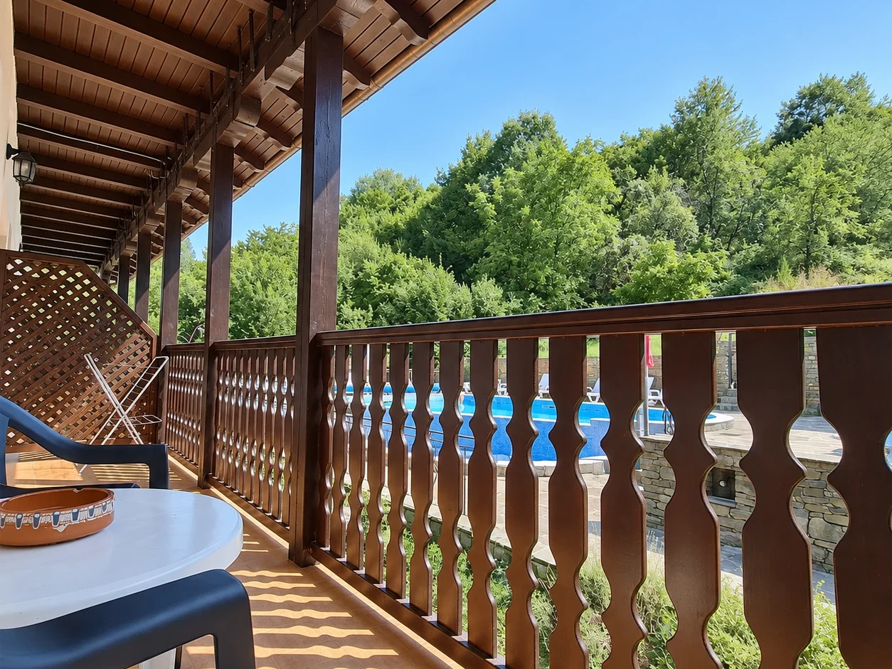 A long balcony with a shaped wooden balustrade under a timber overhang, green trees and a blue sky beyond