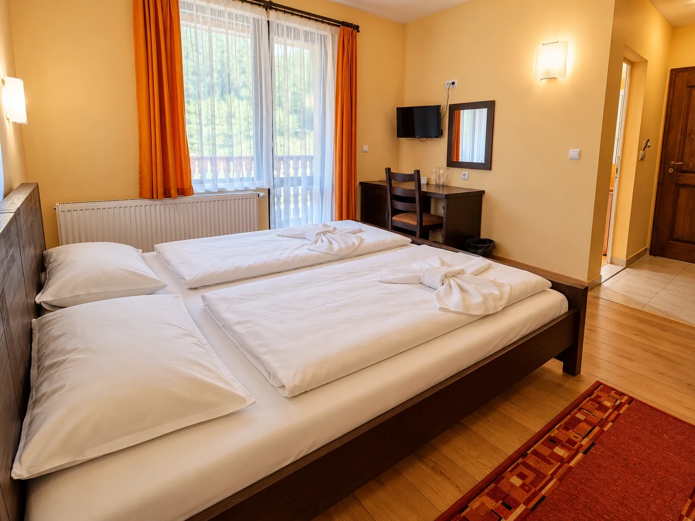 The Double Room with Balcony: a large double bed, a desk and the balcony door with orange curtains