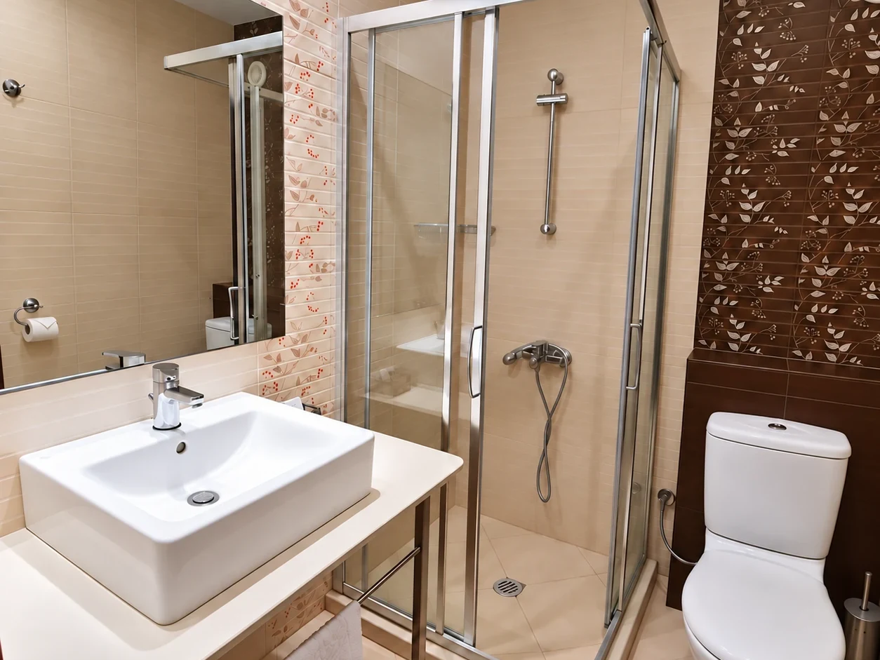 A basin on a pale counter, a shower cubicle and a wall of floral-motif tiles