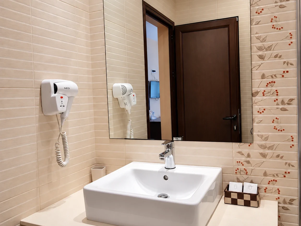 A white basin on a pale counter, a mirror, a wall-mounted hairdryer and floral-motif tiles