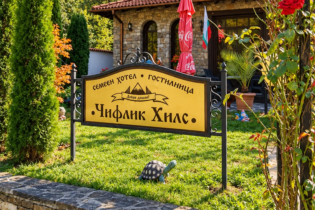 The Chiflik Hills sign in the garden before the hotel, with roses and thujas and the building behind