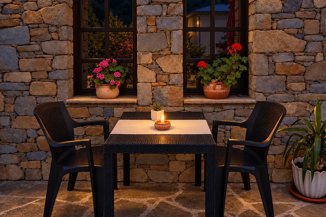 The restaurant terrace in the evening: a stone wall with two arched windows, lit lanterns and a candlelit table for two