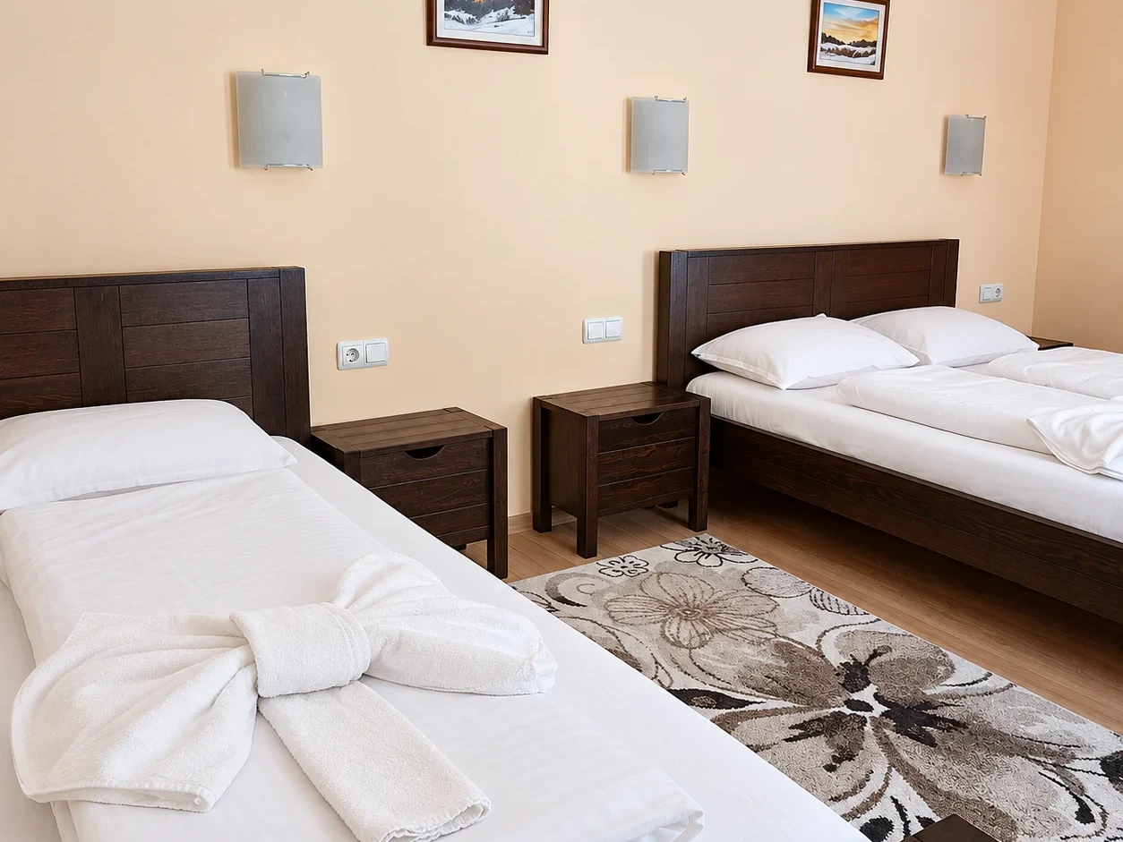 A single and a double bed with dark wooden headboards, bedside tables, wall lamps and a rug with large flowers