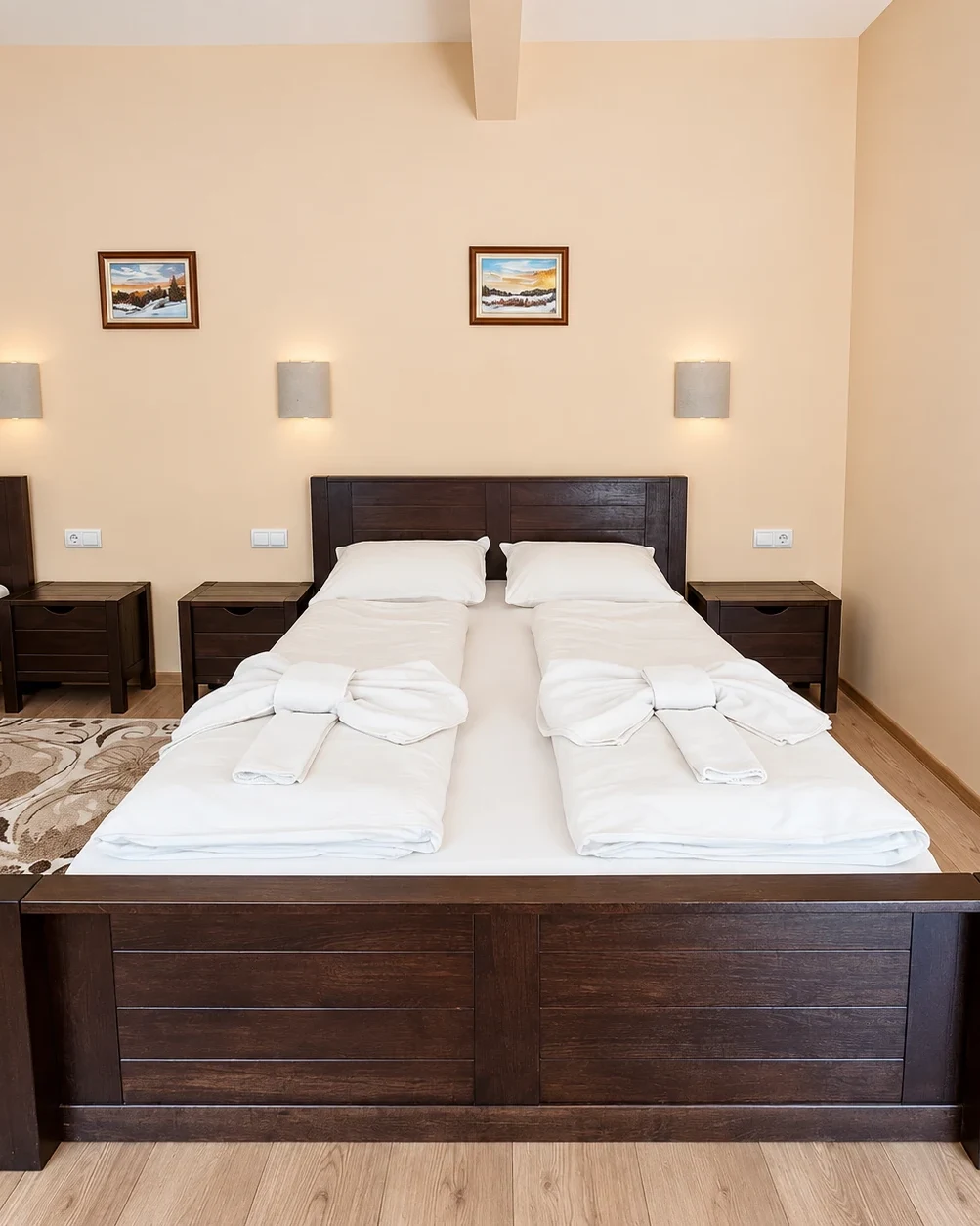 A double bed with a solid wooden footboard and bedside tables, towels folded into knots