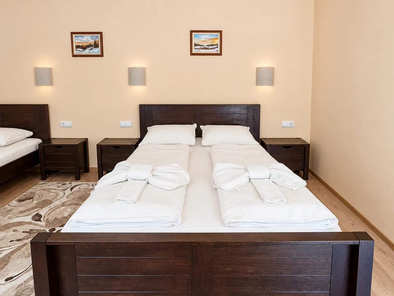 A double bed with a solid wooden footboard and bedside tables, towels folded into knots