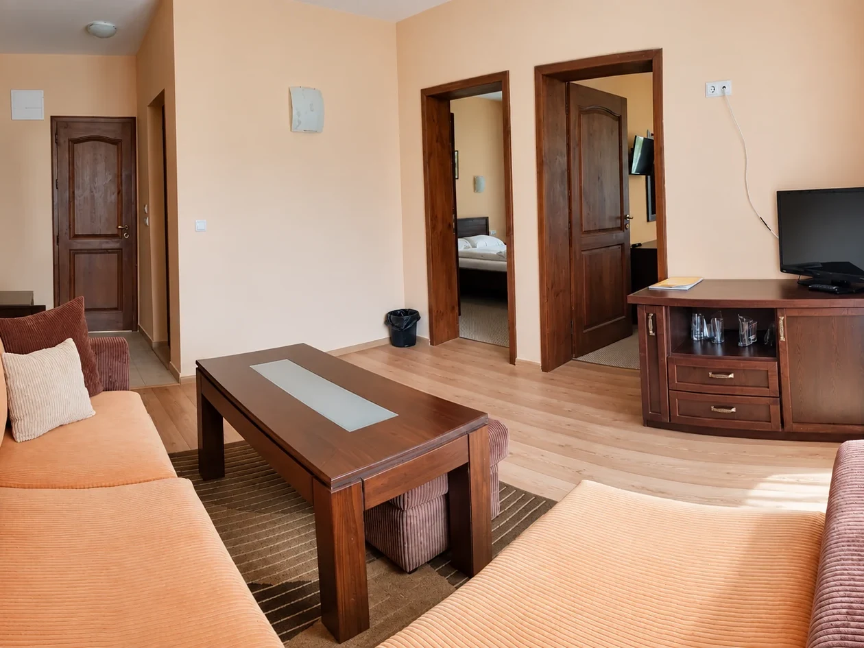 A living room with a sofa, a low table with a glass inlay, a TV on a chest of drawers and doors to both bedrooms