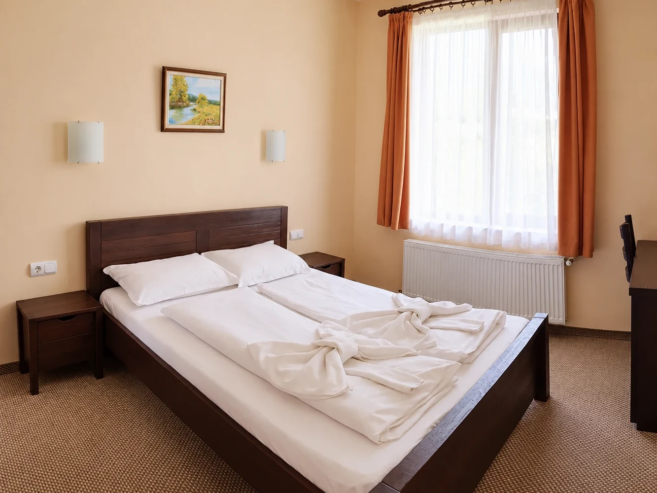 A double bed with a wooden headboard below a window with orange curtains