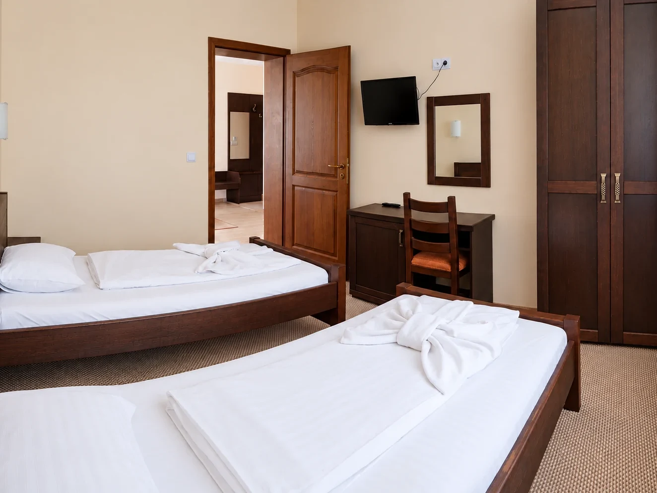 Two single beds with wooden frames, a desk, a wardrobe and an open wooden door